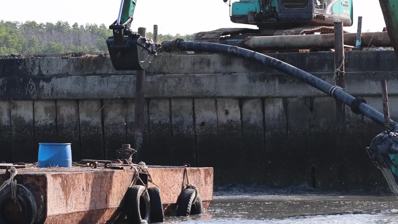 Un escavatore idraulico opera su una chiatta, mostrando il suo braccio meccanico e la benna in un ambiente acquatico.