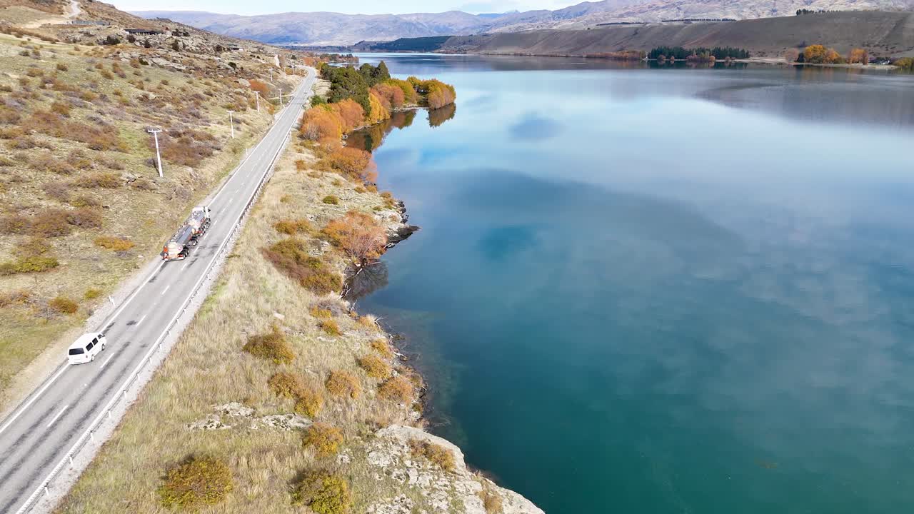 Drone footage captures Lake Dunstan's serene waters and vibrant autumn foliage in Cromwell, New Zealand, under clear skies