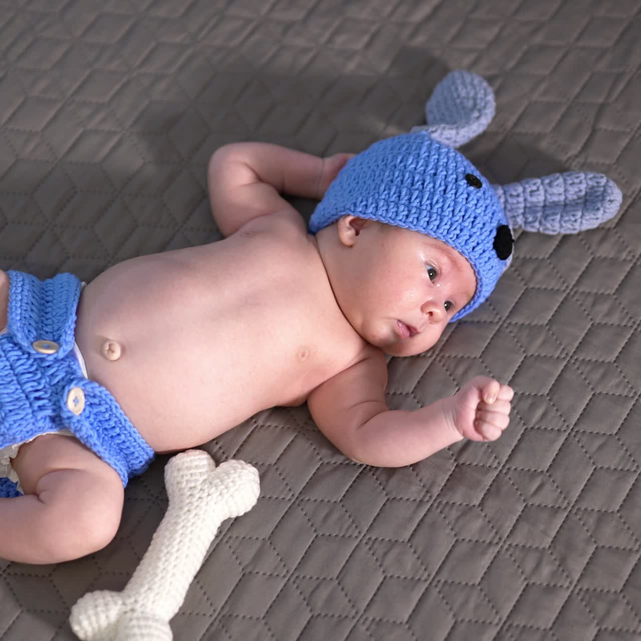 Funny baby boy wearing knitted suit of a puppy. Soft toy bone next to the babe. View from above