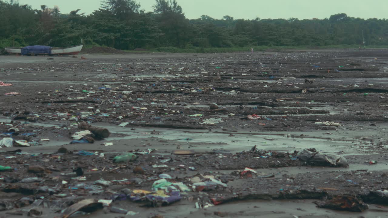 Camera moves closer to sand revealing large amounts of debris scattered across a polluted beach