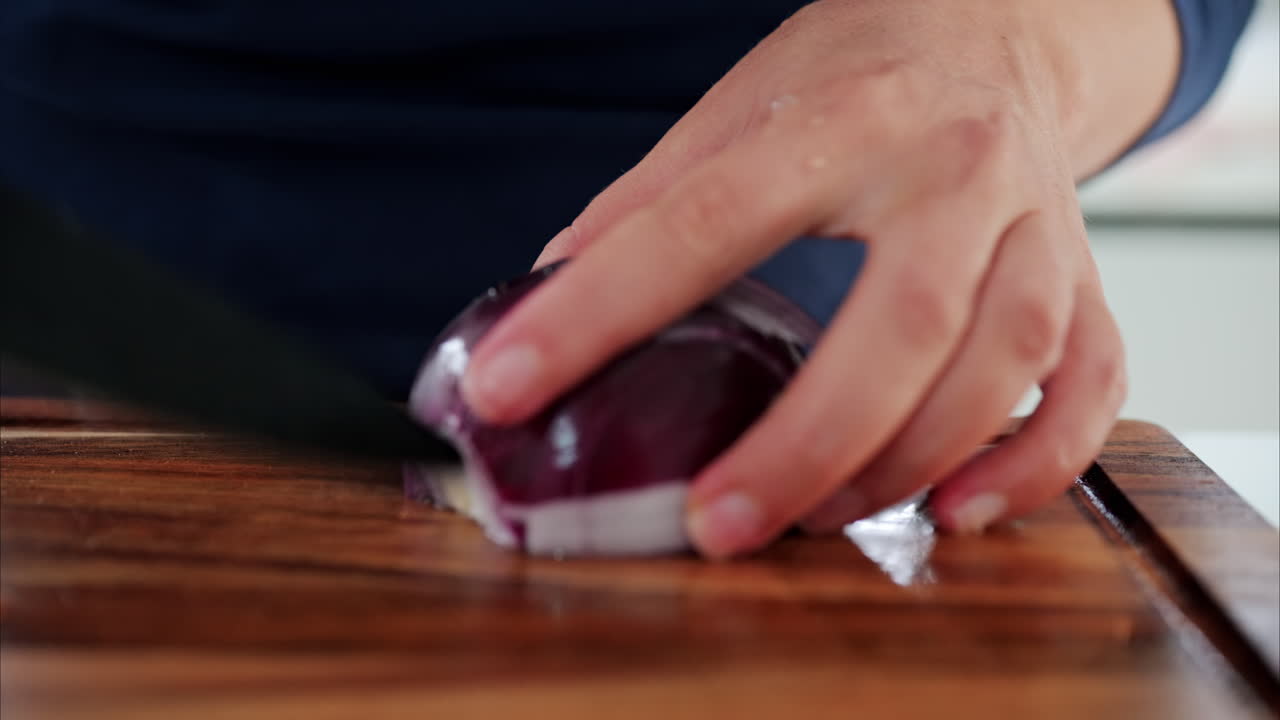 Close up of a woman cutting up a red onion near other vegetables on a wooden cutting board