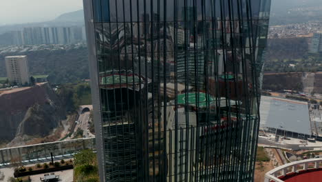 High-angle-view-of-tall-modern-glass-cover-building.-Drone-camera-flying-around-Paradox-Torre-skyscraper.-Glossy-facade-reflecting-surrounding-buildings.-Mexico-City,-Mexico.