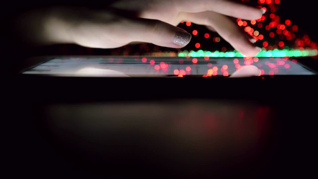 Woman Hand Touching And Browsing On Tablet Device In Dark Room With Colorful Blurry Fiber Optic Lights Closeup Vertical Tilt Motion