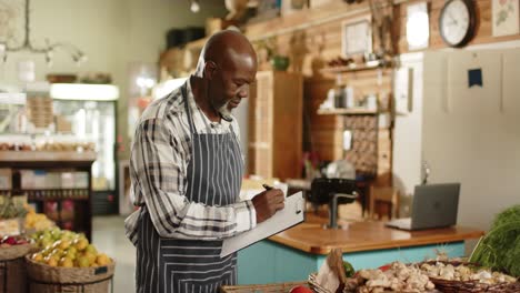 happy senior african american male shopkeeper making inventory at health food shop, slow motion