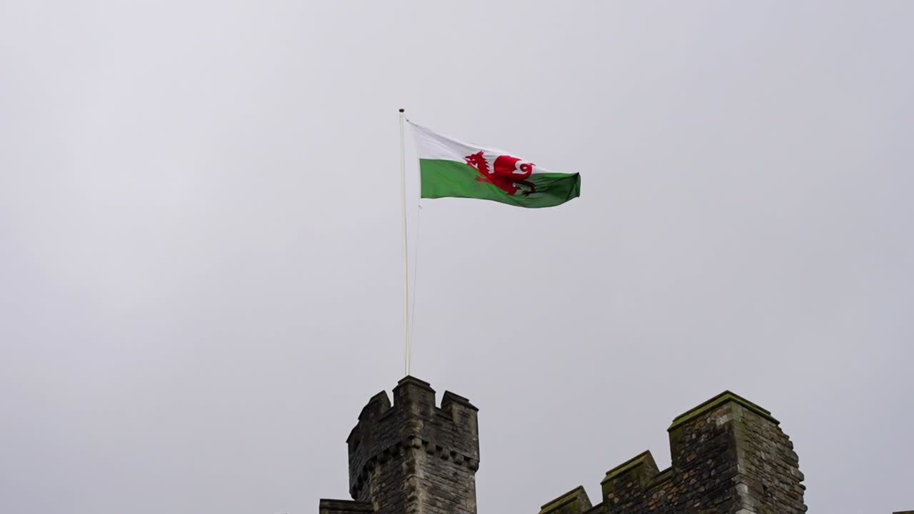 bandera galesa volando en una torre del castillo en cámara lenta, vista contra el cielo nublado