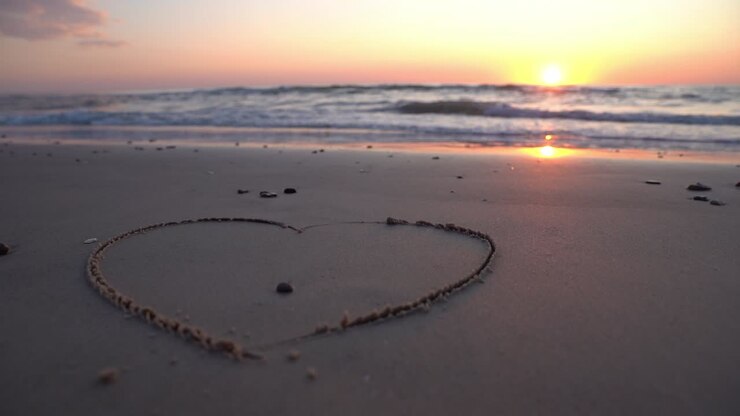 Hart symbool getekend in het zand tegen een achtergrond van zonsondergang boven de zee