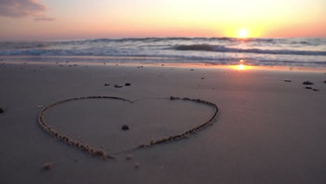 Heart-symbol-drawn-on-sand-against-a-backdrop-of-sunset-over-the-sea