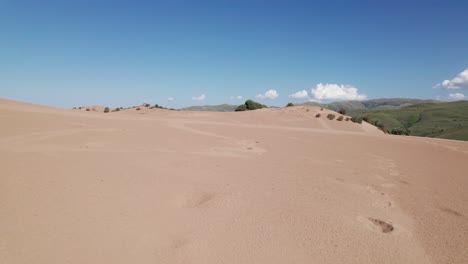 aerial dolly tilt up above epic dunes with foot steps in golden sand