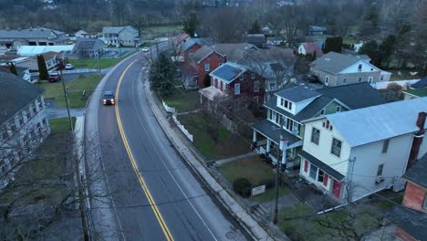 drone establishing shot of white car driving on main road in small american town at dusk