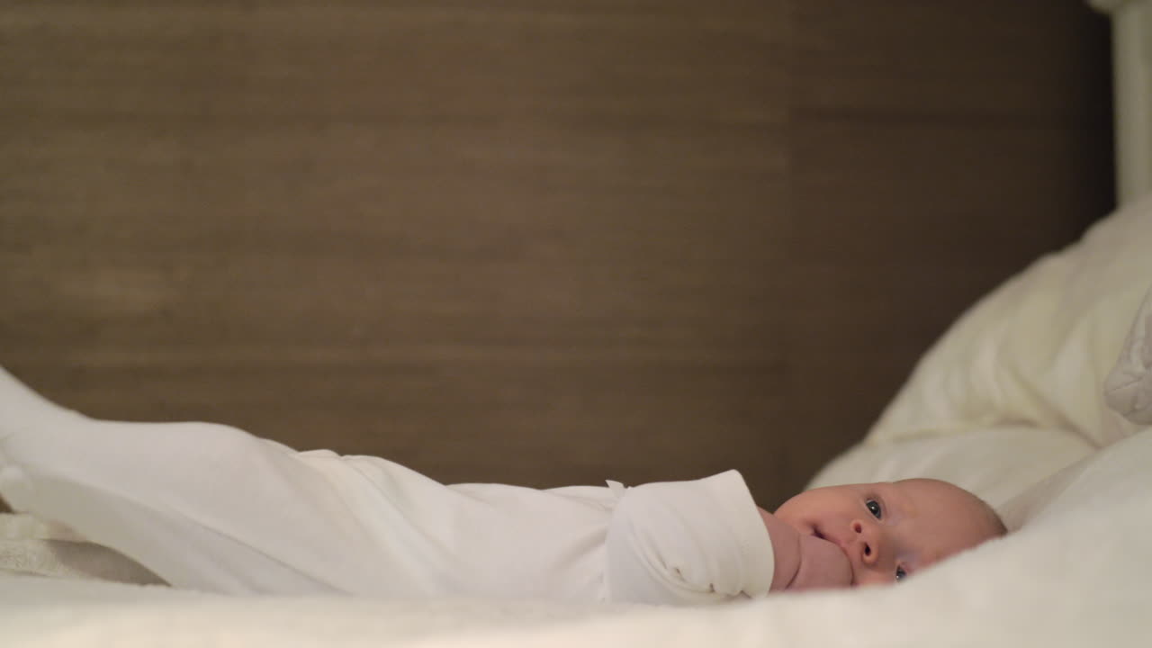 Quiet baby with hand in the mouth lying on big bed
