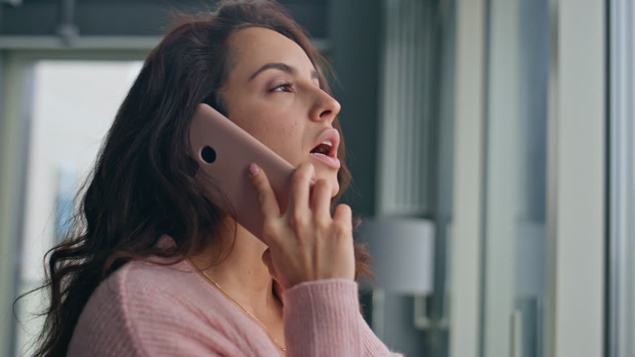 걱정하는 여성이 큰 창문에서 드폰으로 전화합니다. 집 근접. 긴장한 소녀 전화