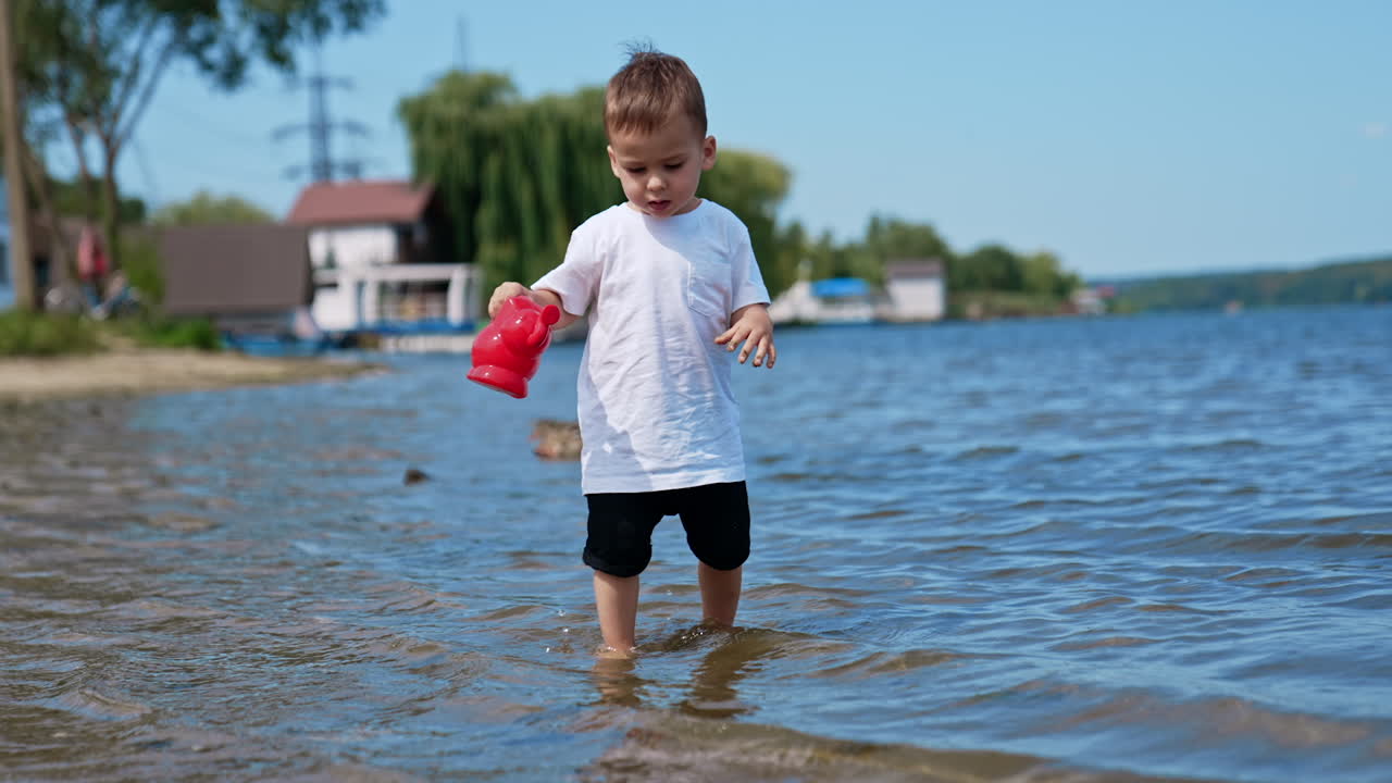 Cute baby boy plays with a watering can. Toddler tries to fill the can. Child playing in the beach.