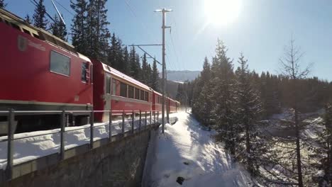 Drohnenaufnahmen-Aus-Der-Luft-Mit-Einem-Leuchtend-Roten-Zug,-Der-Durch-Ein-Schneebedecktes-Wunderland-Gleitet