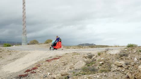 joven madre aventurera luchando con un cochecito en el duro paisaje de tenerife