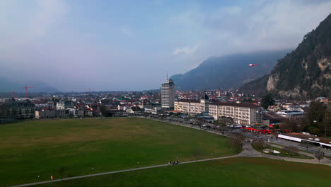 aerial trucking pan flies above grassy open field with view of homes sprawling across interlaken switzerland