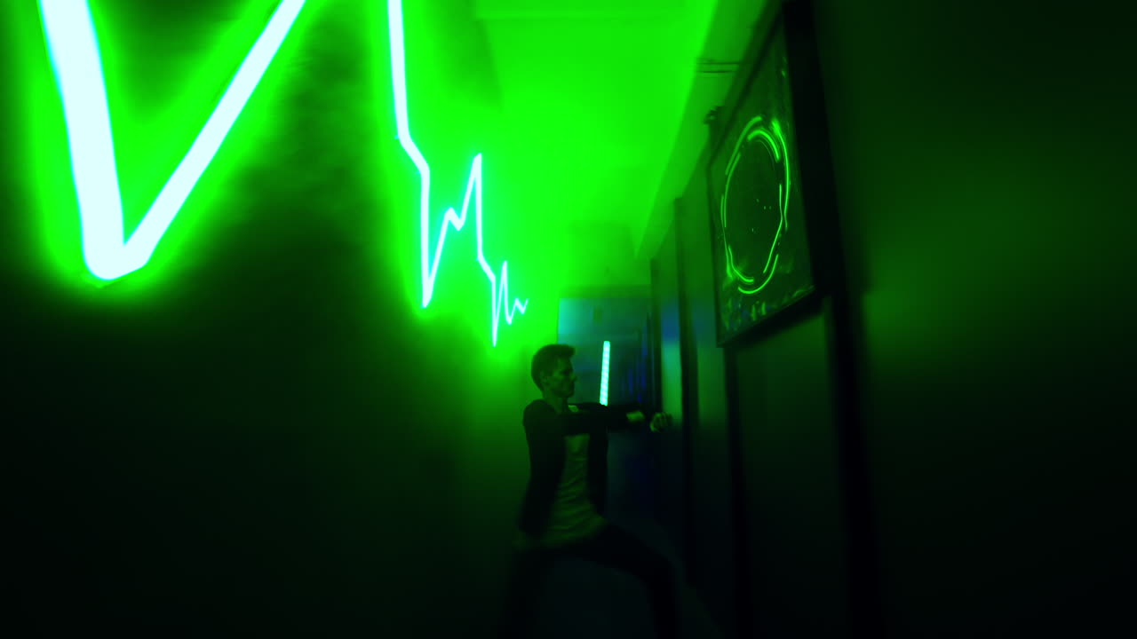 Young man dancing in the dark corridor lit with green light. Hip hop dancer performs in limited space area.