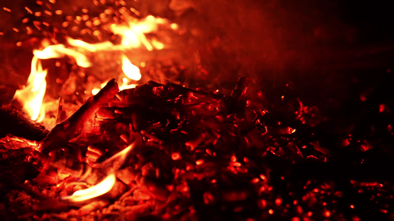 Moving the glowing charcoal in the bonfire. Beautiful flames and sparkles close up.