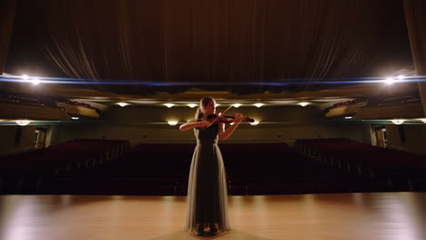 woman playing violin on an empty concert hall stage