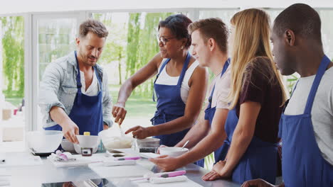 female teacher with male student mixing ingredients for recipe in cookery class in kitchen