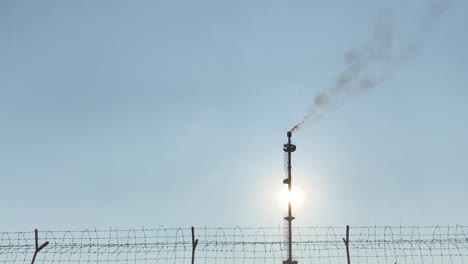 establisher view of gas flare smokestack industry, clear blue sky, pan