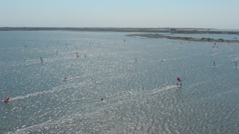 drone - aerial shot of many windsurfers on a blue, wavy and windy sea on a sunny day with white clouds on a island, 25p