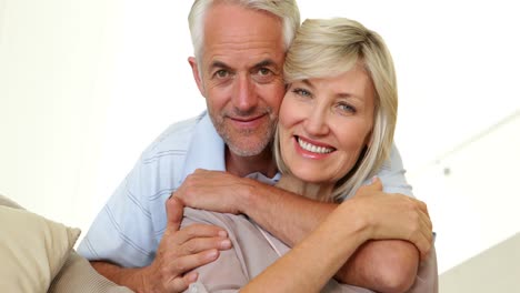 Couple-hugging-on-the-couch-and-smiling-at-camera