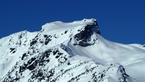 Snowy-Mountain-Summit-And-Blue-Sky-In-Winter---aerial-shot