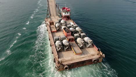 barge loaded with concrete mixer trucks pulled to port by a tugboat in hong kong bay, aerial view