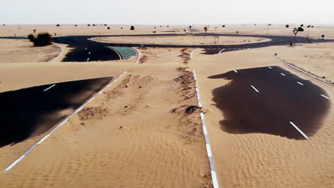 an aerial of a road in a desert with the sand partially covering it up. forward movement.