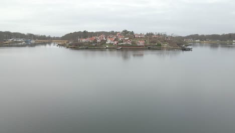 a tranquil shot flying over the still water in karlskrona, sweden with the beautiful picturesque island of brandaholm in the background, with its famous red cabins