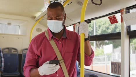 hombre afroamericano en la ciudad con máscara facial, usando un teléfono inteligente en el autobús