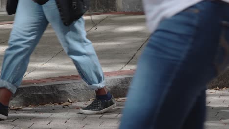 cierre la toma en cámara lenta de las piernas y los pies de las personas mientras caminan arriba y abajo por una concurrida acera en el centro de la ciudad durante un descanso para almorzar en un día laboral normal
