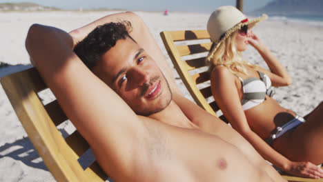 caucasian couple sitting on sunbeds on the beach