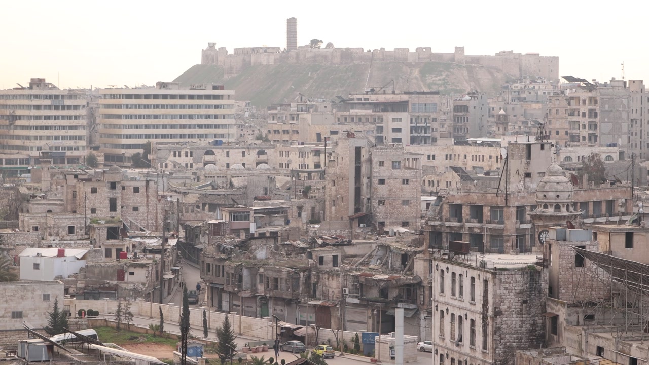 Wide, hazy panoramic view over the skyline of Aleppo, Syria. Traditional minarets and urban sprawl visible through the dust of the historic city