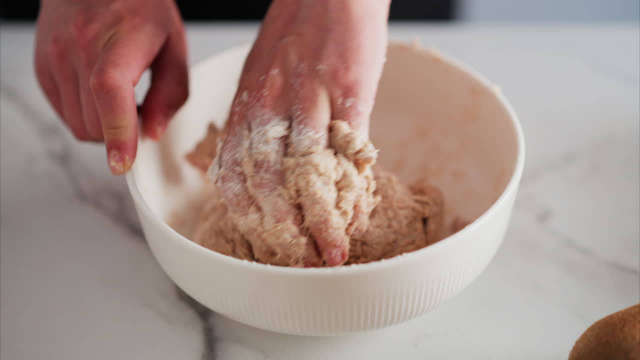 Close up of a woman's hands kneading dough in a white bowl