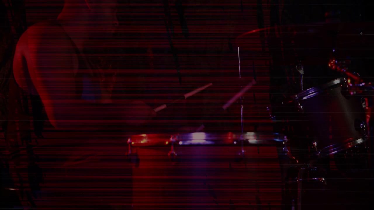 Batterista uomo che suona la batteria su un palco musicale poco illuminato, i colpi delle bacchette causano scanline ed effetto mosso.