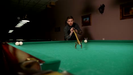un primer plano de un hombre jugando al billar en un bar oscuro, golpea la pelota con un taco.