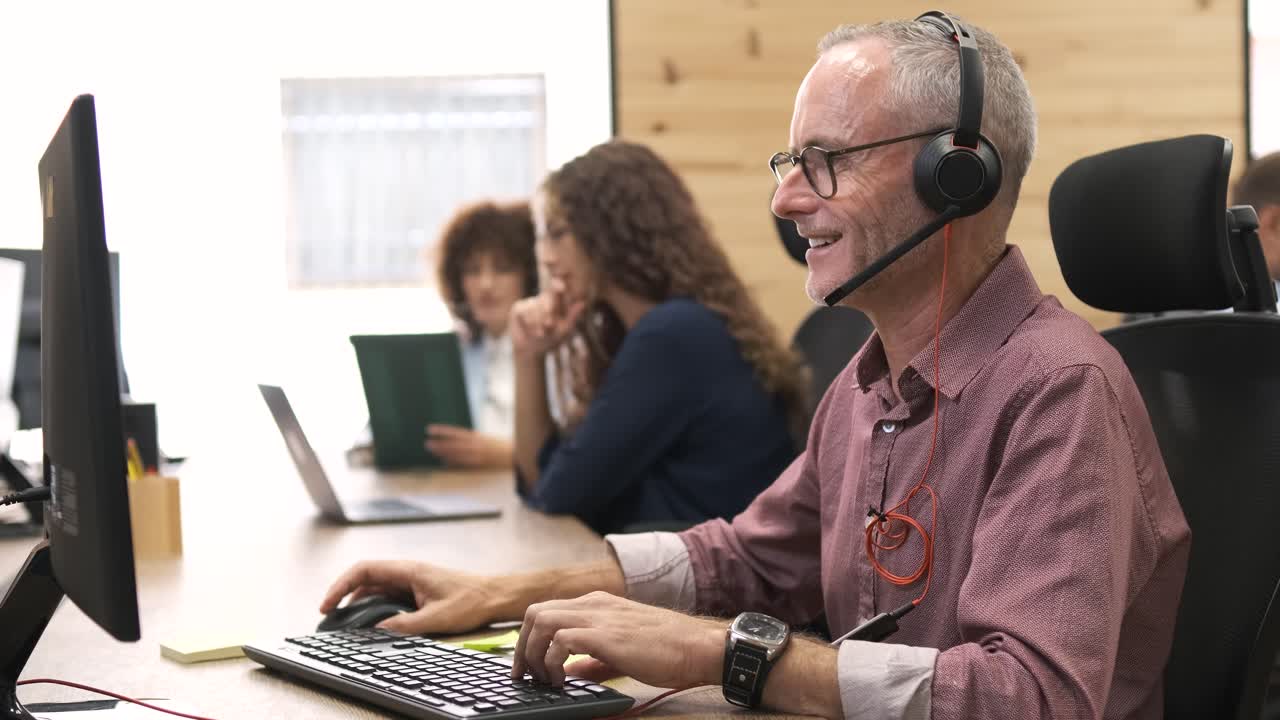 Happy mature businessman talking through headset in coworking office