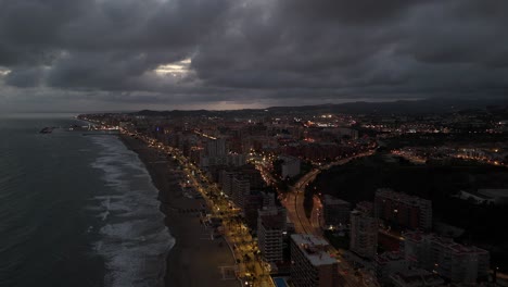 drone capturing torreblanca, spain, at dusk, showing illuminated streets and buildings under a dramatic cloudy sky, offering a breathtaking aerial perspective, orbiting over the mediterranean sea