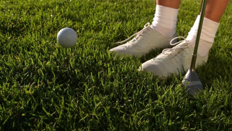 la pelota de golf cayendo al lado de los pies y el club de las golfistas