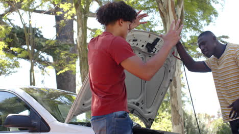 Checking car engine, two multiracial male friends discussing maintenance outdoors