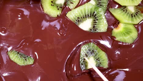 kiwi slices being dipped into chocolate sauce