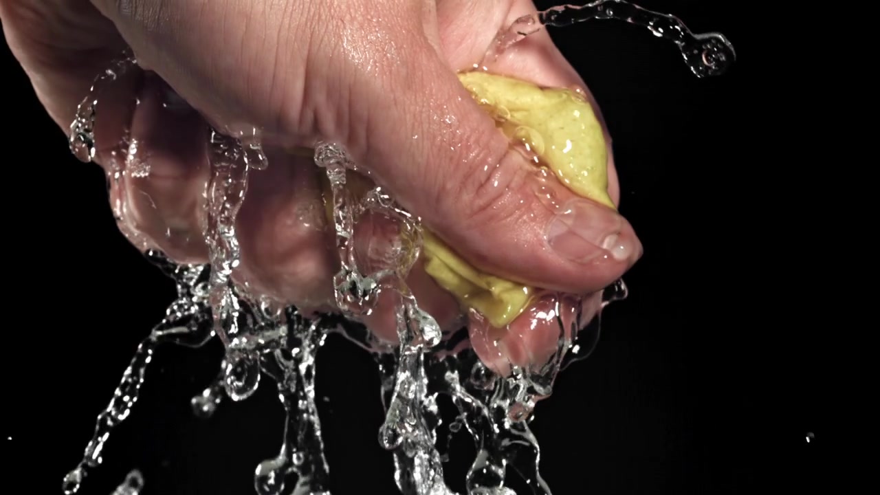 Mano exprimiendo esponja amarilla mojada con agua goteando en cámara lenta