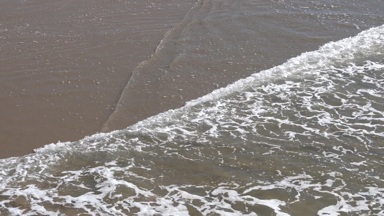 Calming ocean water overlapping over wet sand in 4K. Aerial view.