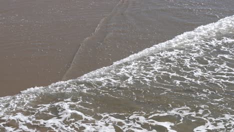 calming ocean water overlapping over wet sand in 4k. aerial view.