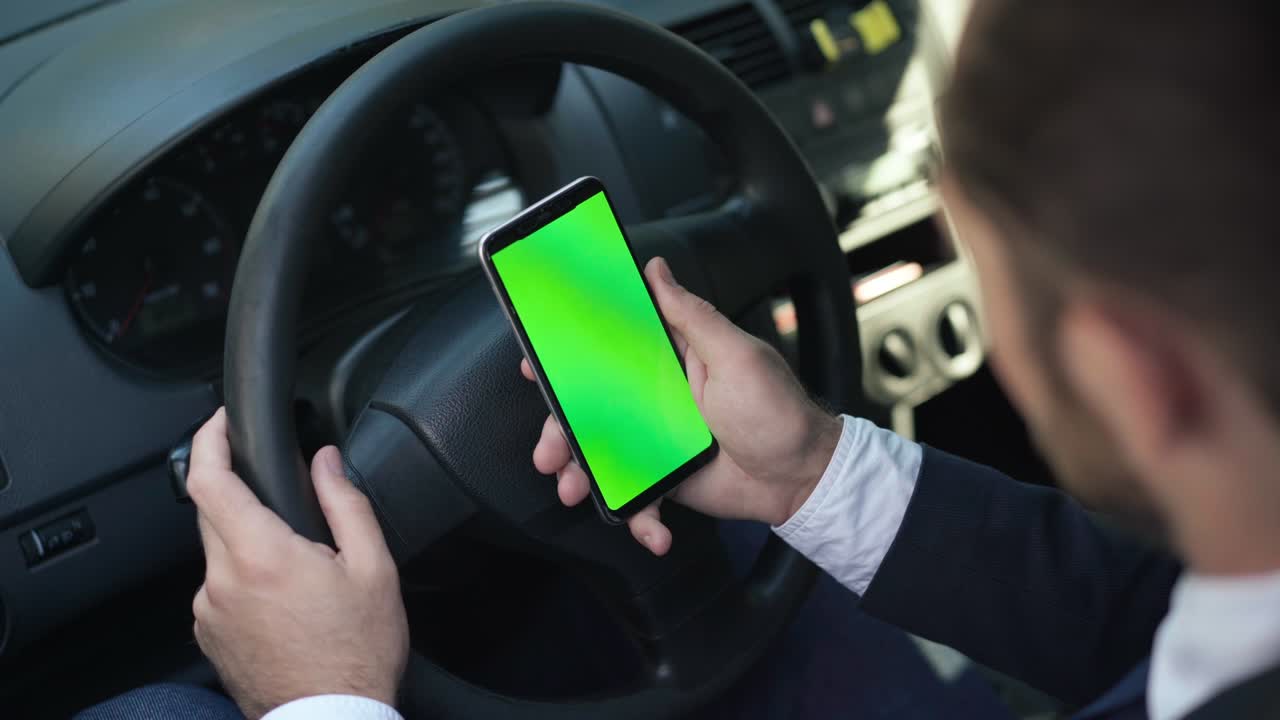 smartphone de pantalla verde de primer plano en mano caucásica masculina en el volante. joven borroso irreconocible en traje viendo el sitio web sentado en un automóvil en el asiento del conductor. maqueta de plantilla.