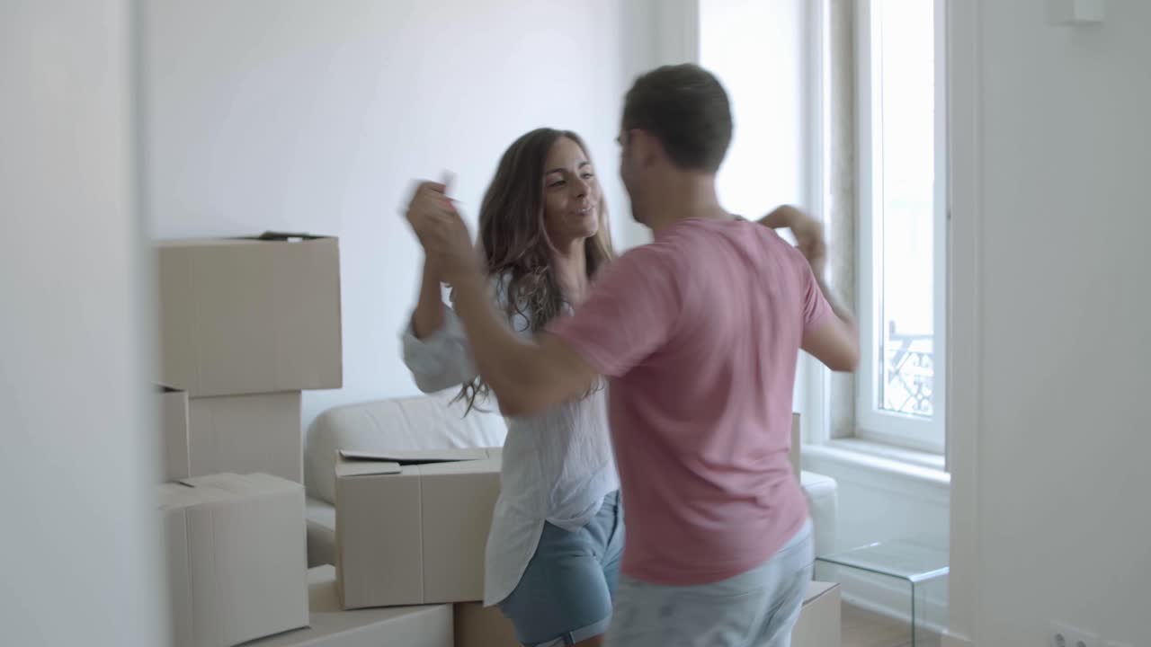 casal caucasiano feliz se mudando para uma casa nova, dançando e se divertindo na sala de estar com caixas
