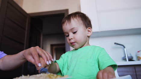 lovely toddler eating from form. mom helps him to pick up food from plate. low angle view.