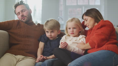 family at home with children sitting on sofa watching tv together as parents fall asleep