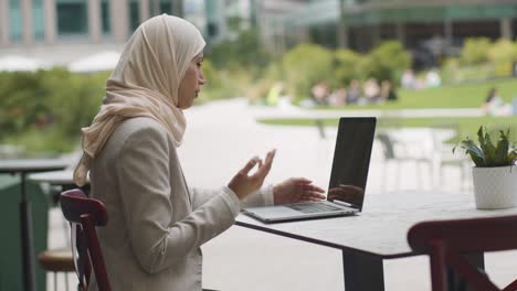 muslim businesswoman sitting outdoors in city gardens making video call on laptop 1